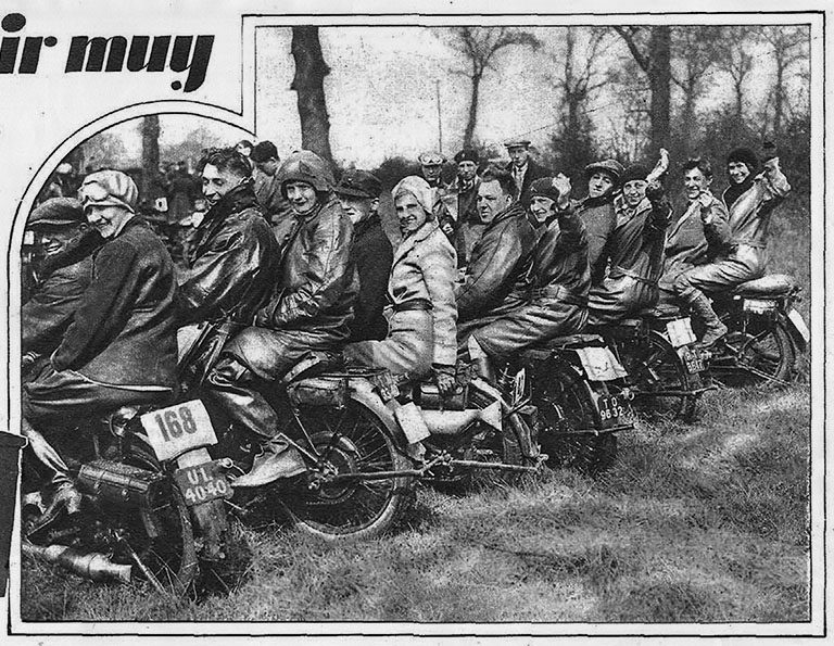 Un grupo de hombres y mujeres que miran a la cámara riendo, montados y montadas en sus motocicletas en un entorno natural, que parece ser un bosque.